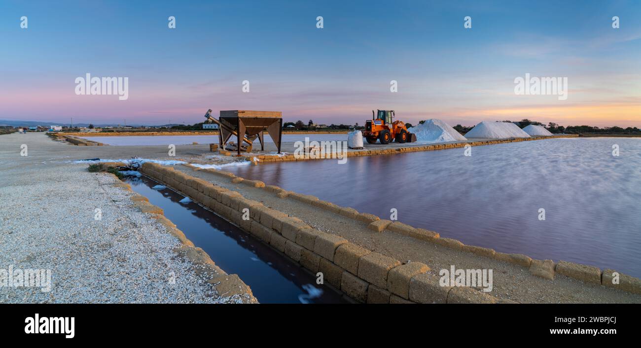 Paceco, Italy - 3 January, 2024: front loader and piles of sea salt in the salt flat of Trapani and Paceco at sunset Stock Photo