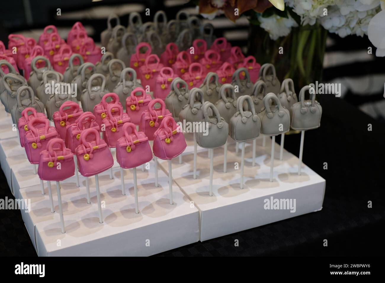 Rows of designer handbag lollypop cakes, the Hermes Birkin bag and Givenchy Antigona bag cake pops with a vase flowers Stock Photo