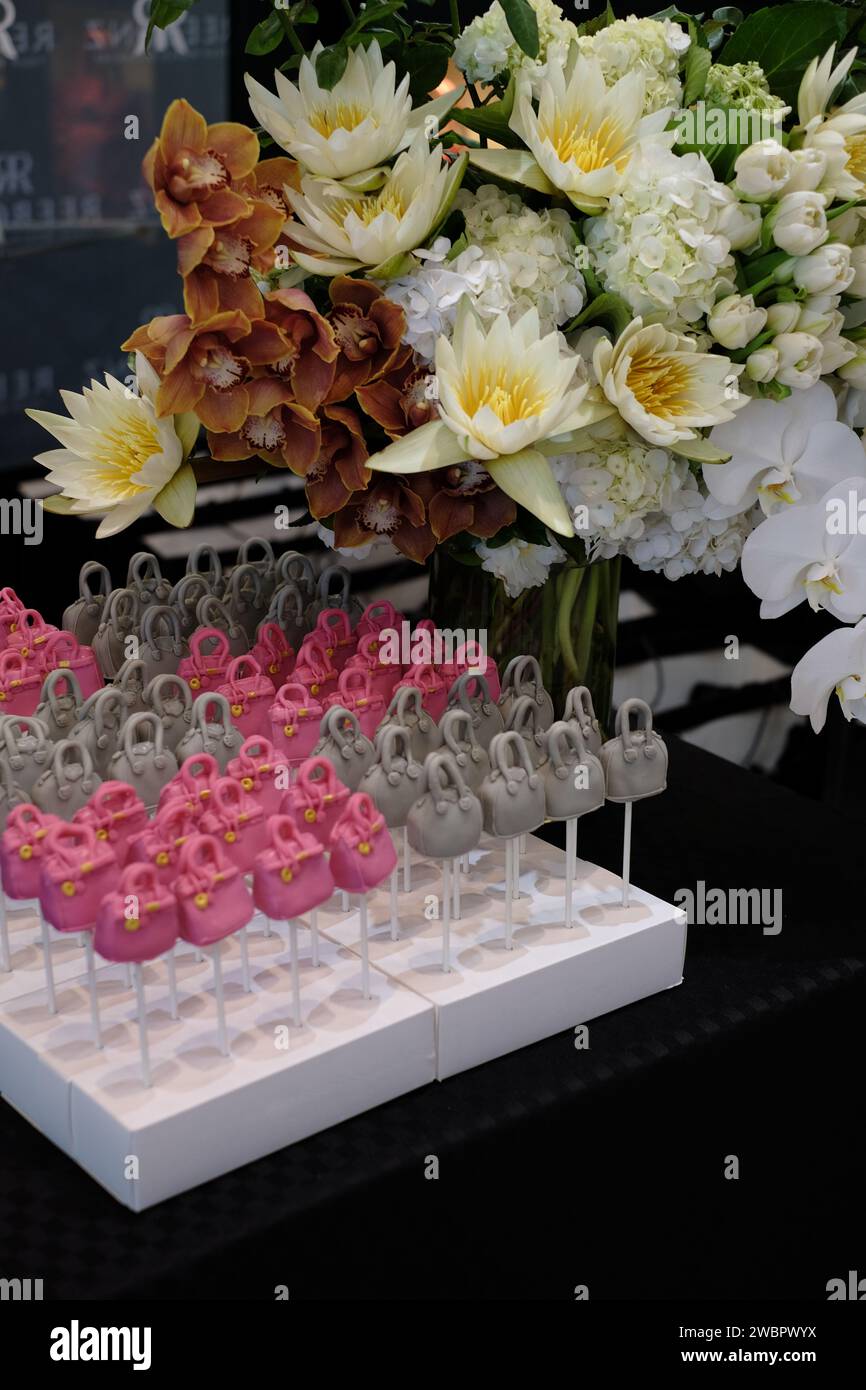Rows of designer handbag lollypop cakes, the Hermes Birkin bag and Givenchy Antigona bag cake pops with a vase of White Water Lilly flowers Stock Photo