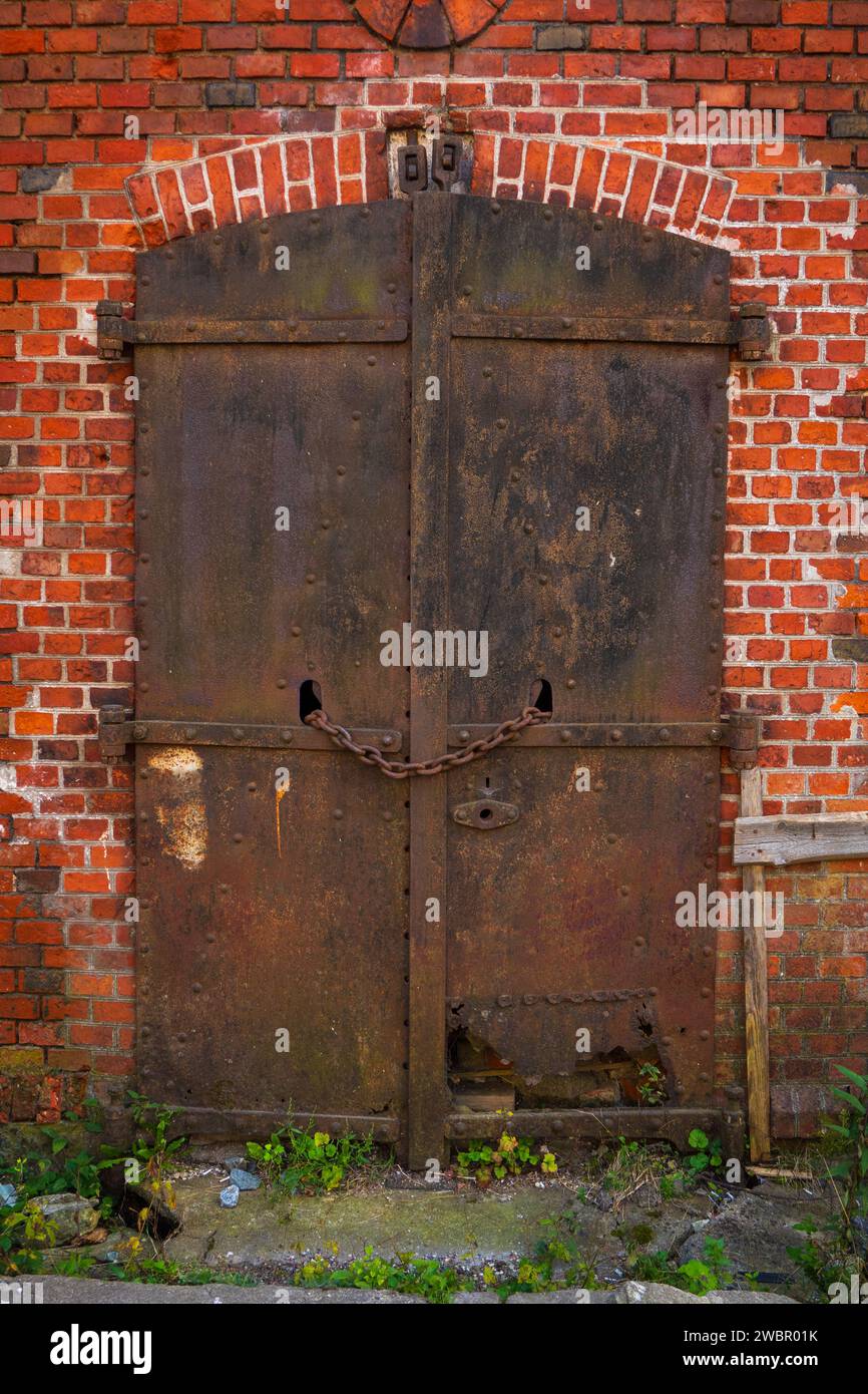 Rusted metal doors on a brick wall, locked with a chain, hinting at ...