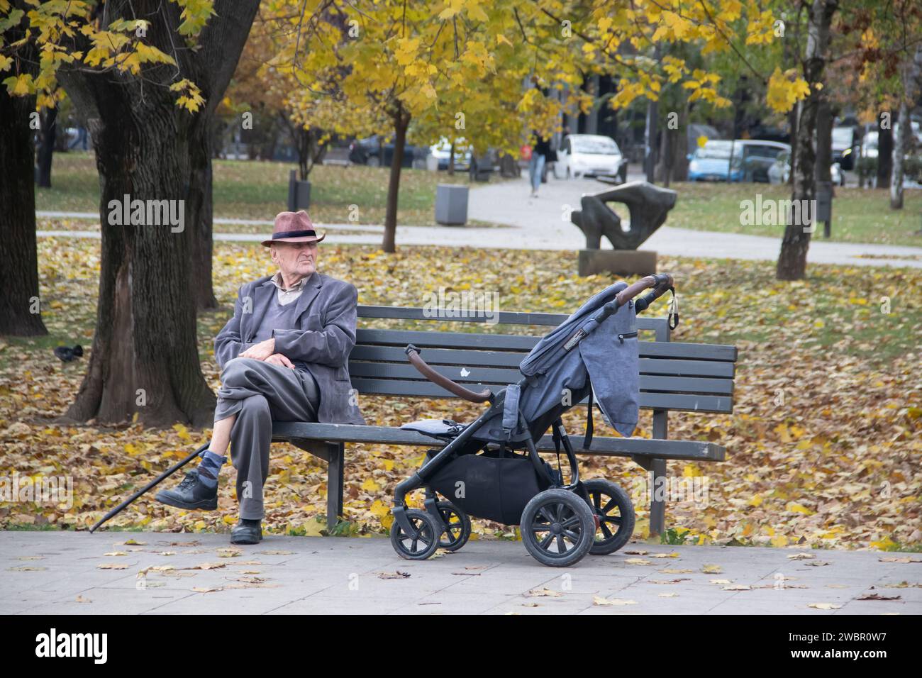 Grandfather taking grandchild for a walk resting at the bench in public city park Stock Photo