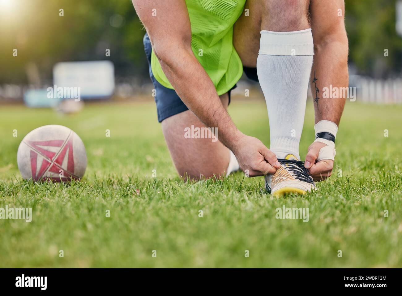 Rugby ball, hands and tying shoe lace on grass field getting ready for ...