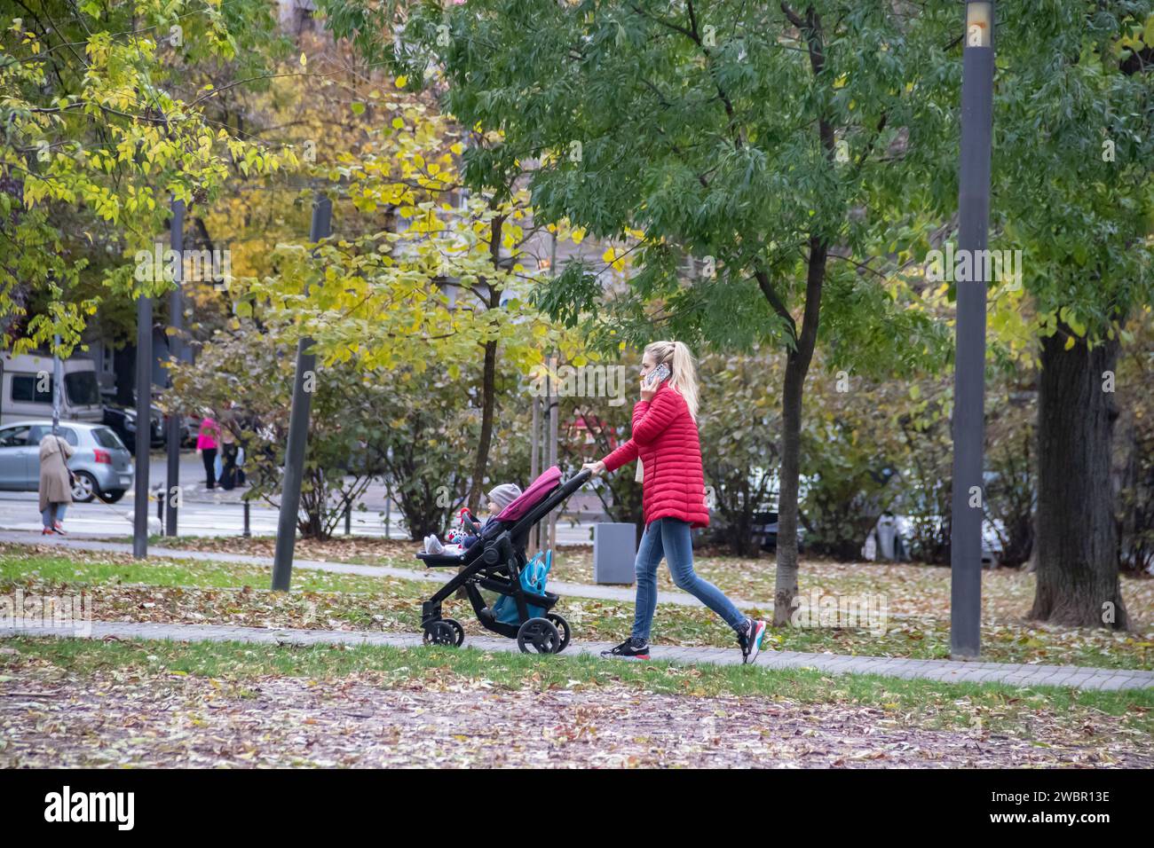 Young parent (mama) taking her child to the public children park at autumn time in October Stock Photo