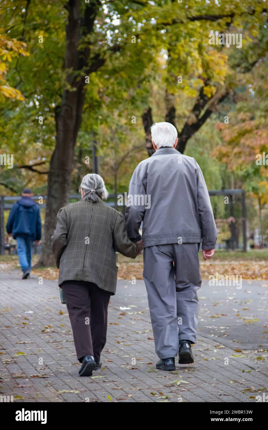 Elder retired couple taking a walk in public city park at autumn time, everlasting love Stock Photo