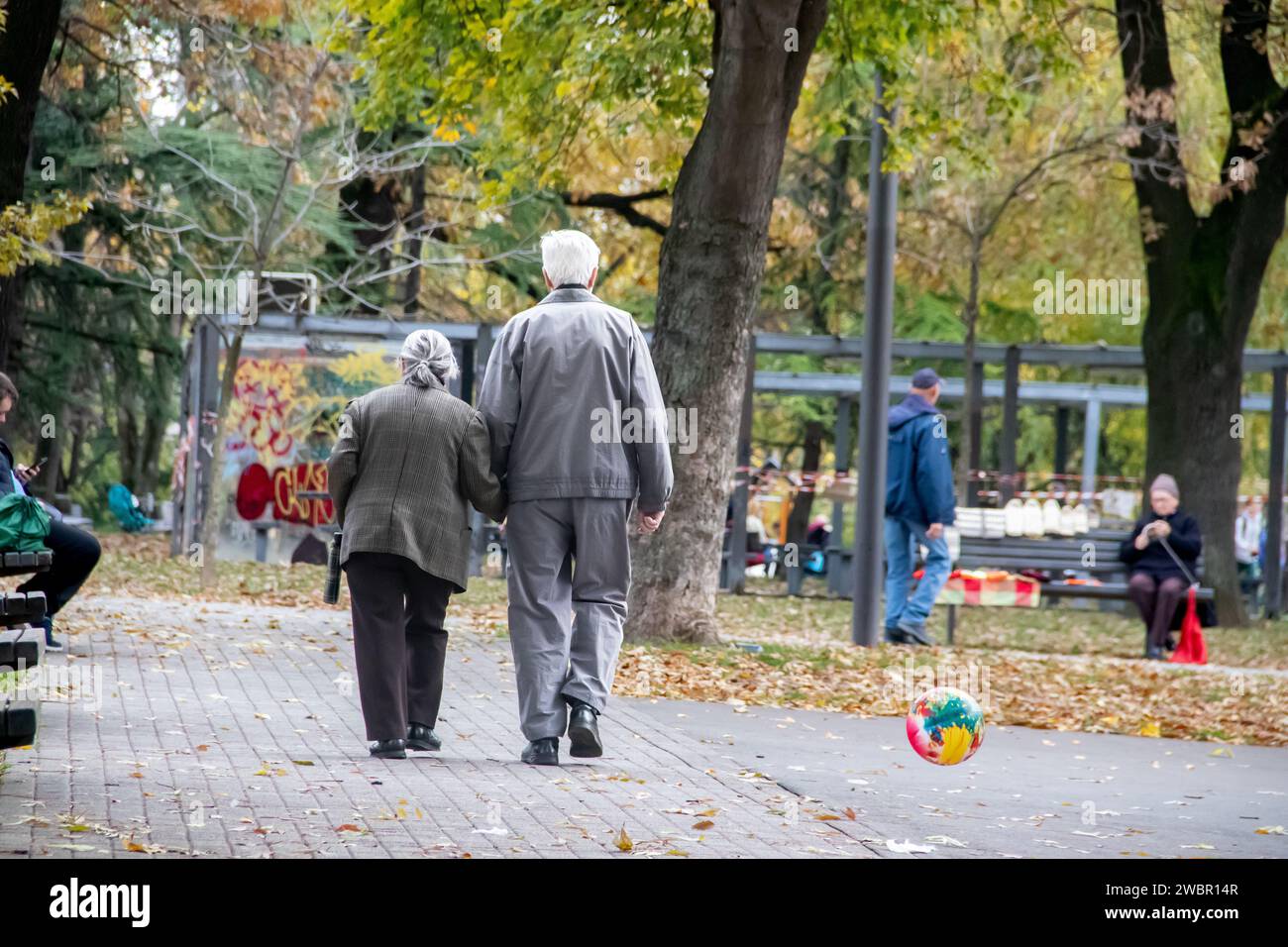 Elder retired couple taking a walk in public city park at autumn time, everlasting love Stock Photo