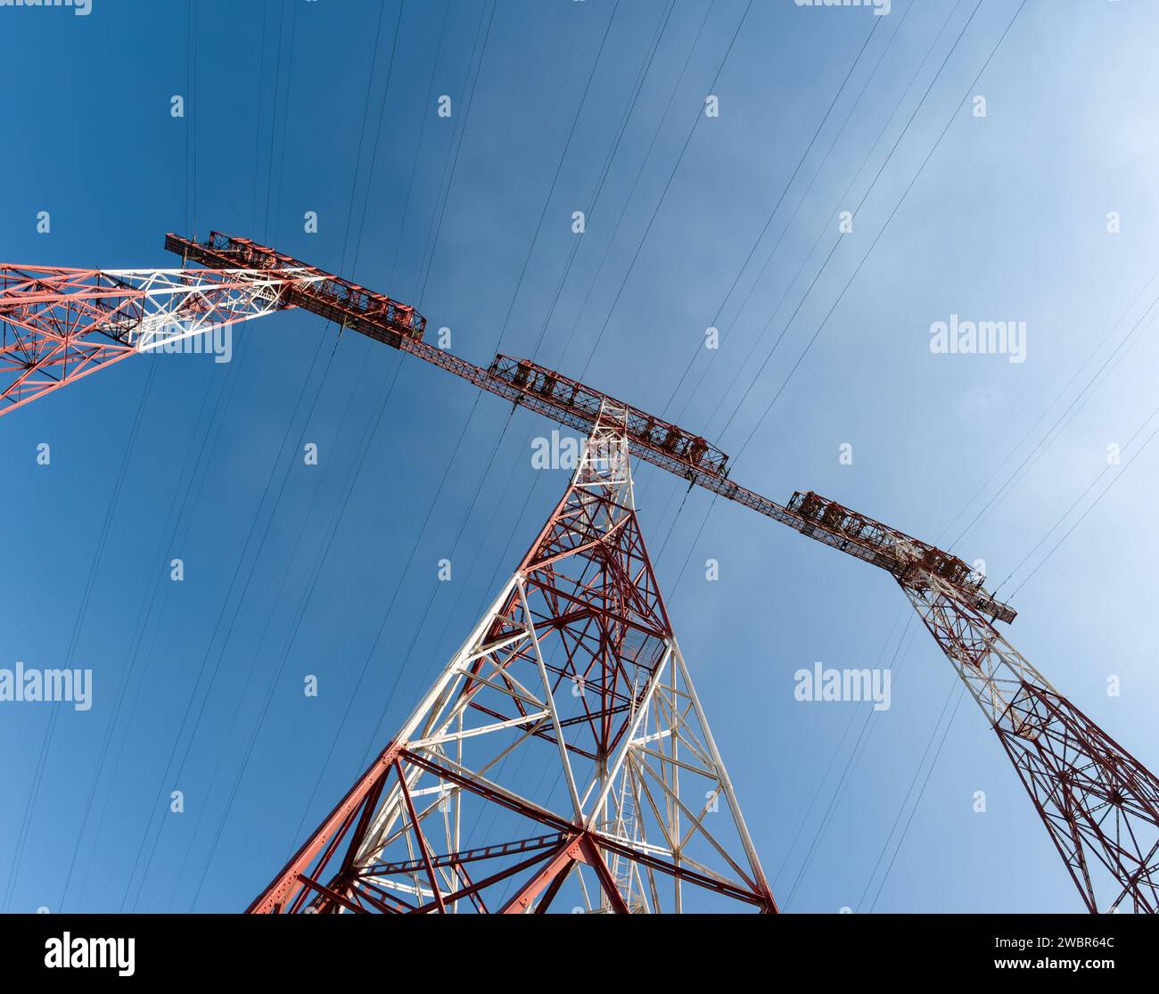 Very tall electrical towers for transmitting high voltage current from a power plant against a blue sky background, shot with an ultra-wide-angle lens Stock Photo