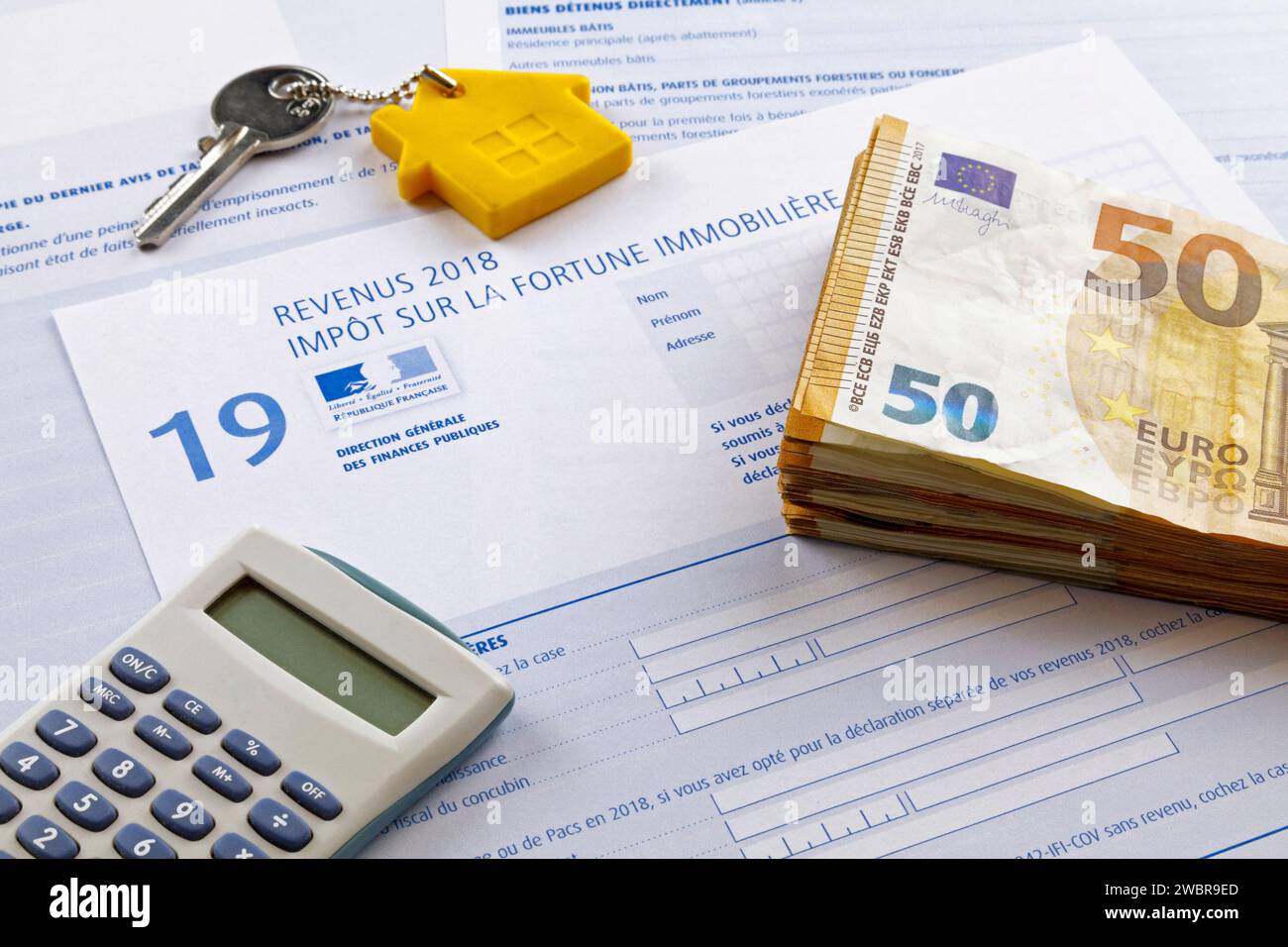Stack of 50 euro banknotes, a home key and a calculator on the top of a French Property wealth tax form (Impôt sur la fortune immobilière). Stock Photo