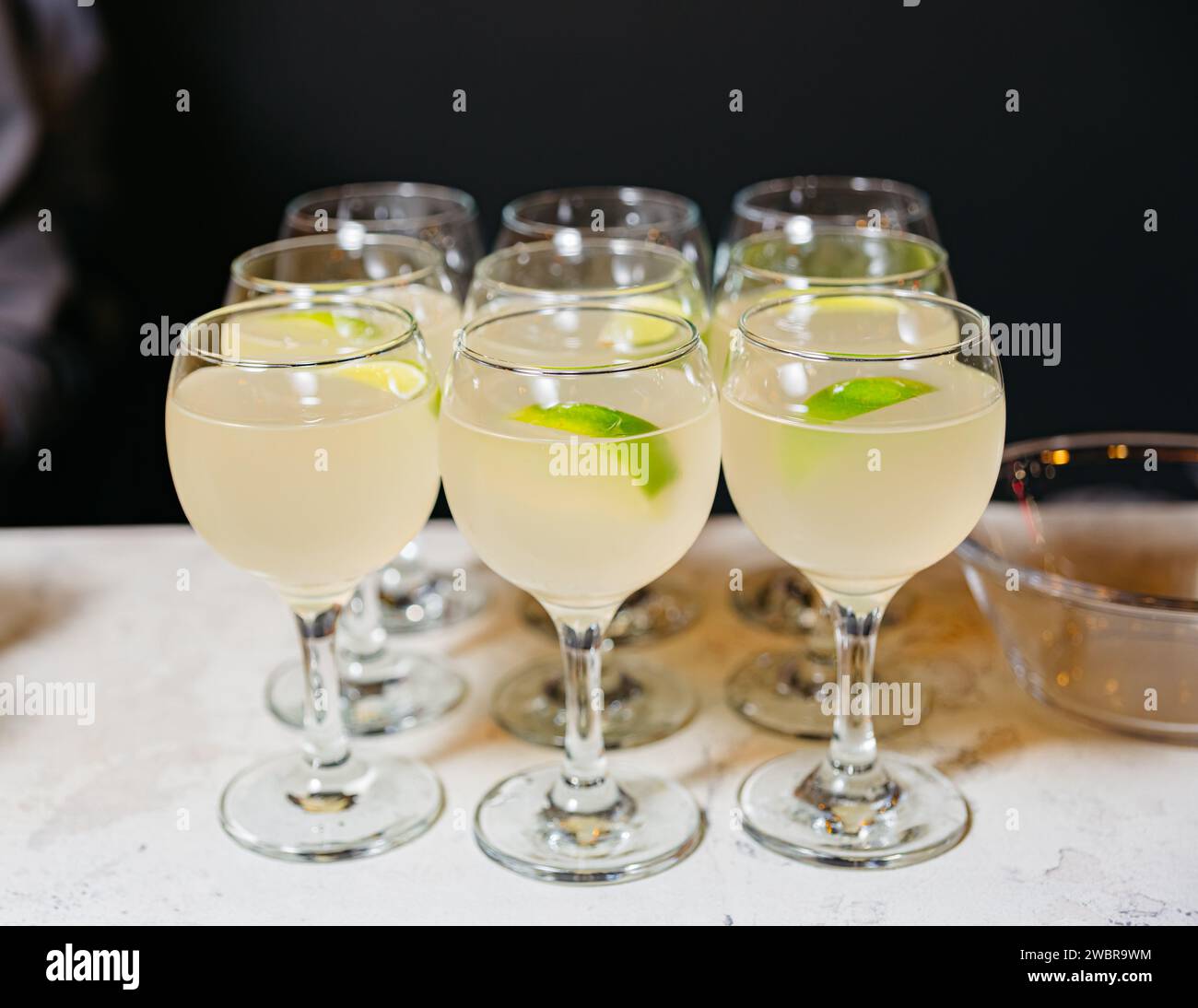 Elegant stemmed glasses filled with a cloudy lemon-lime cocktail, accented with fresh lime garnishes against a dark background. Stock Photo