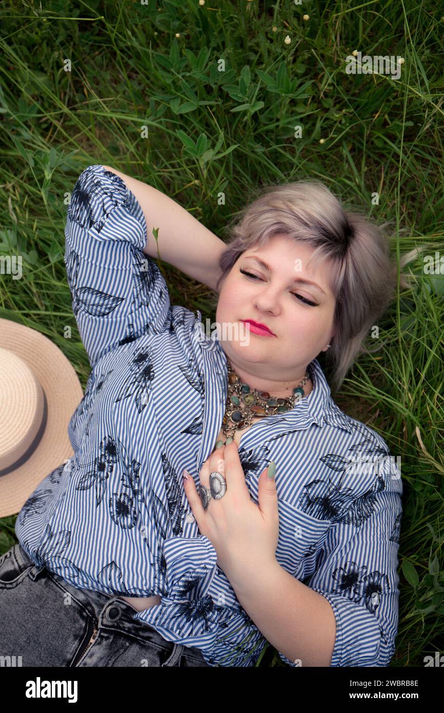 young fat woman with a hat is lying in the grass, top view Stock Photo