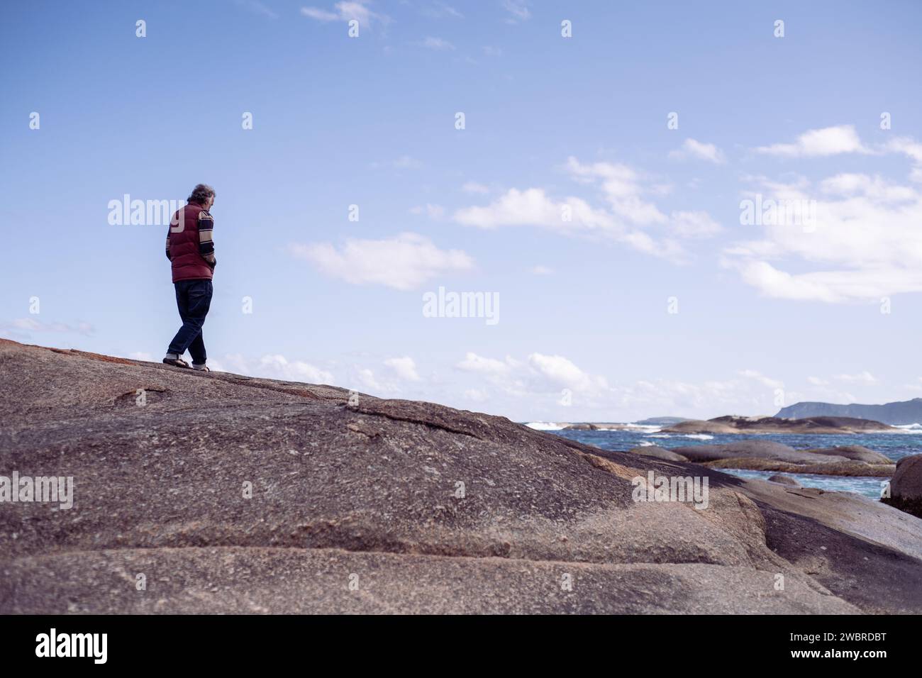 senior retired man walks along boulder in ocean alone Stock Photo