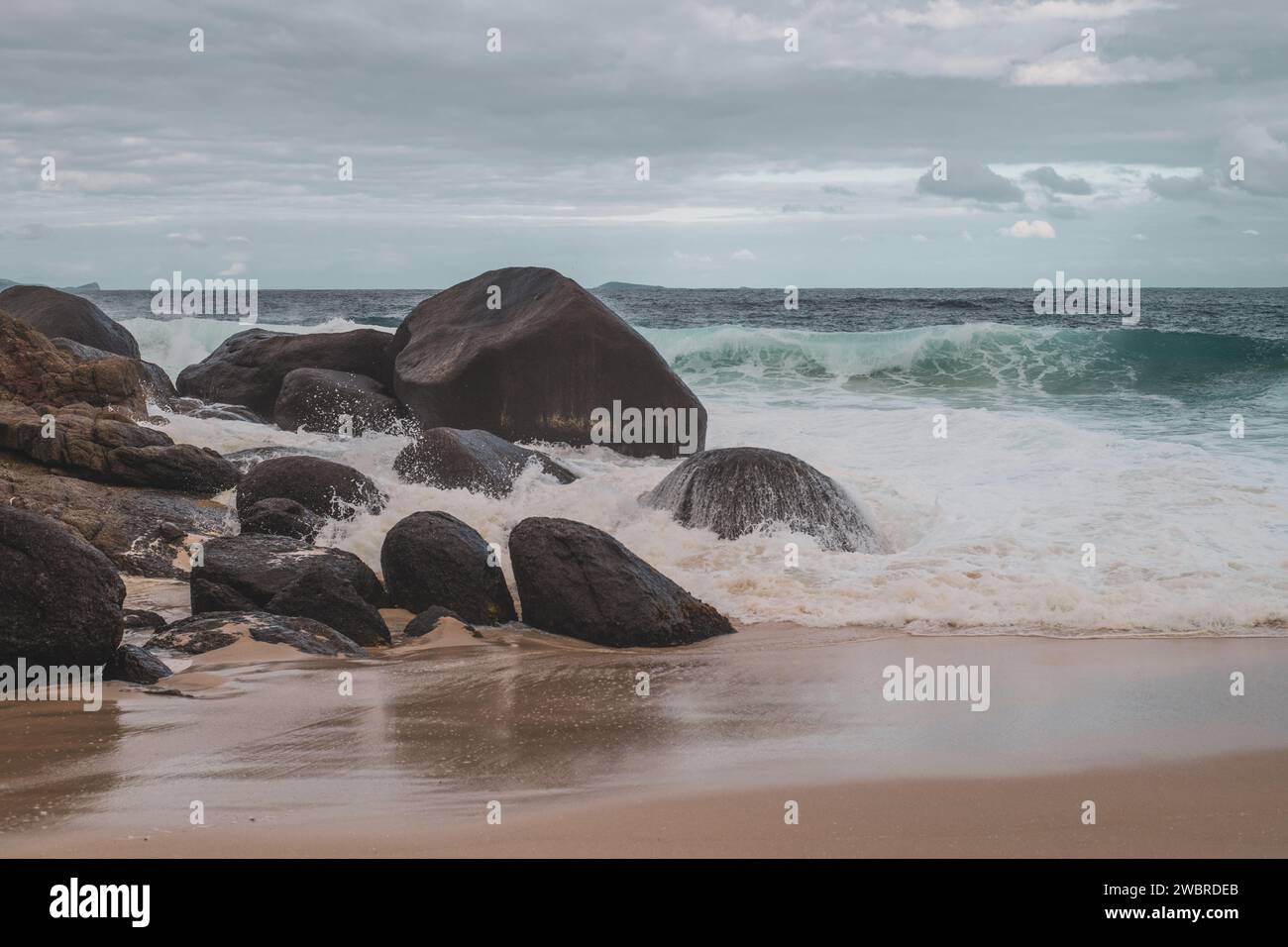 waves crash onto boulders in remote stormy beach in australia Stock Photo