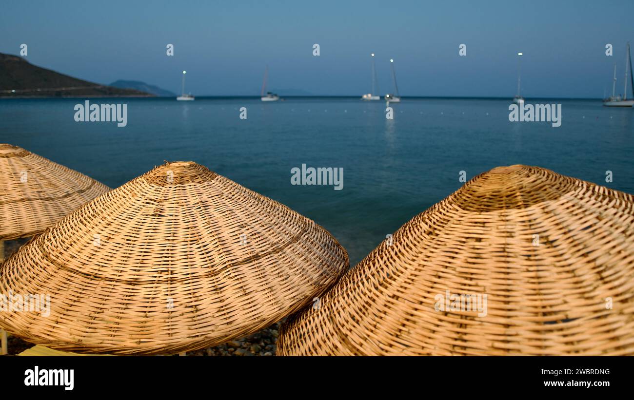 Aegean and Mediterranean coasts at sunset. Wicker umbrellas and sun loungers. Beach restaurants. Palamutbuku beaches of Mugla, Turkiye. Stock Photo
