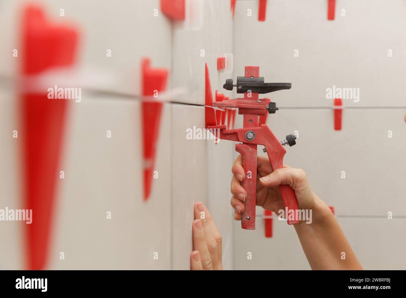 Woman tiling bathroom walls. Flat wall plastic tile leveling system