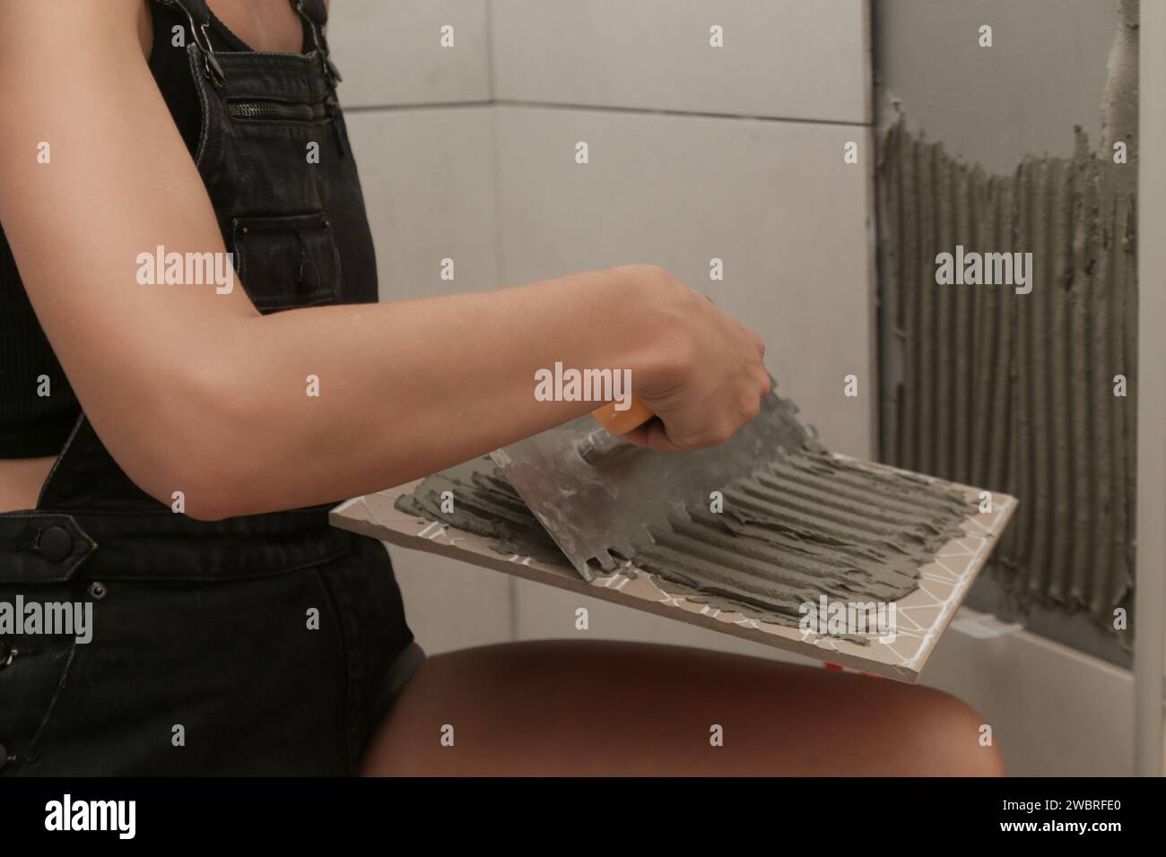 Woman tiling bathroom walls, applying adhesive on a tile and placing