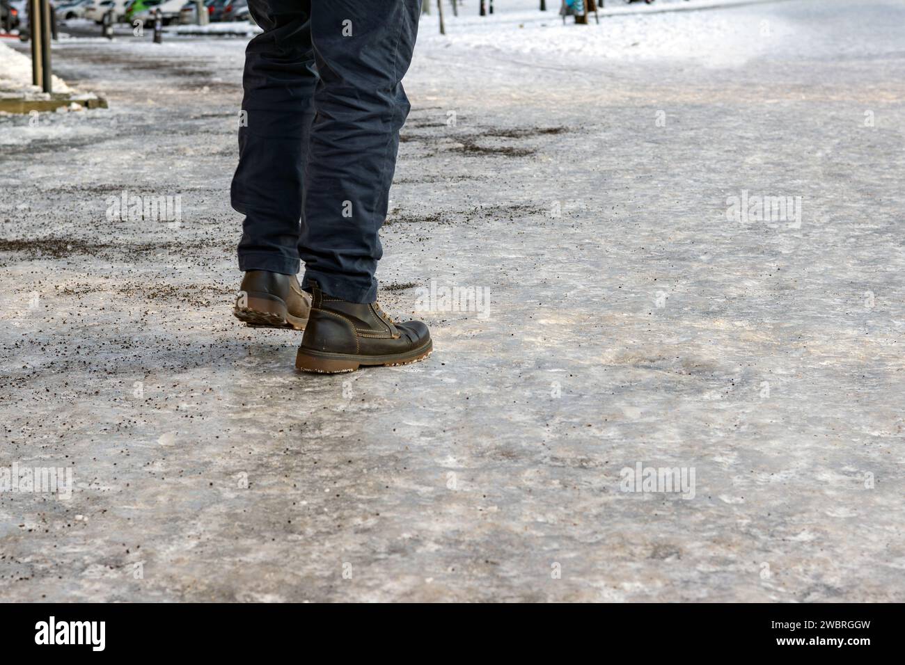 man walks on dangerously icy sidewalks with little grit Stock Photo