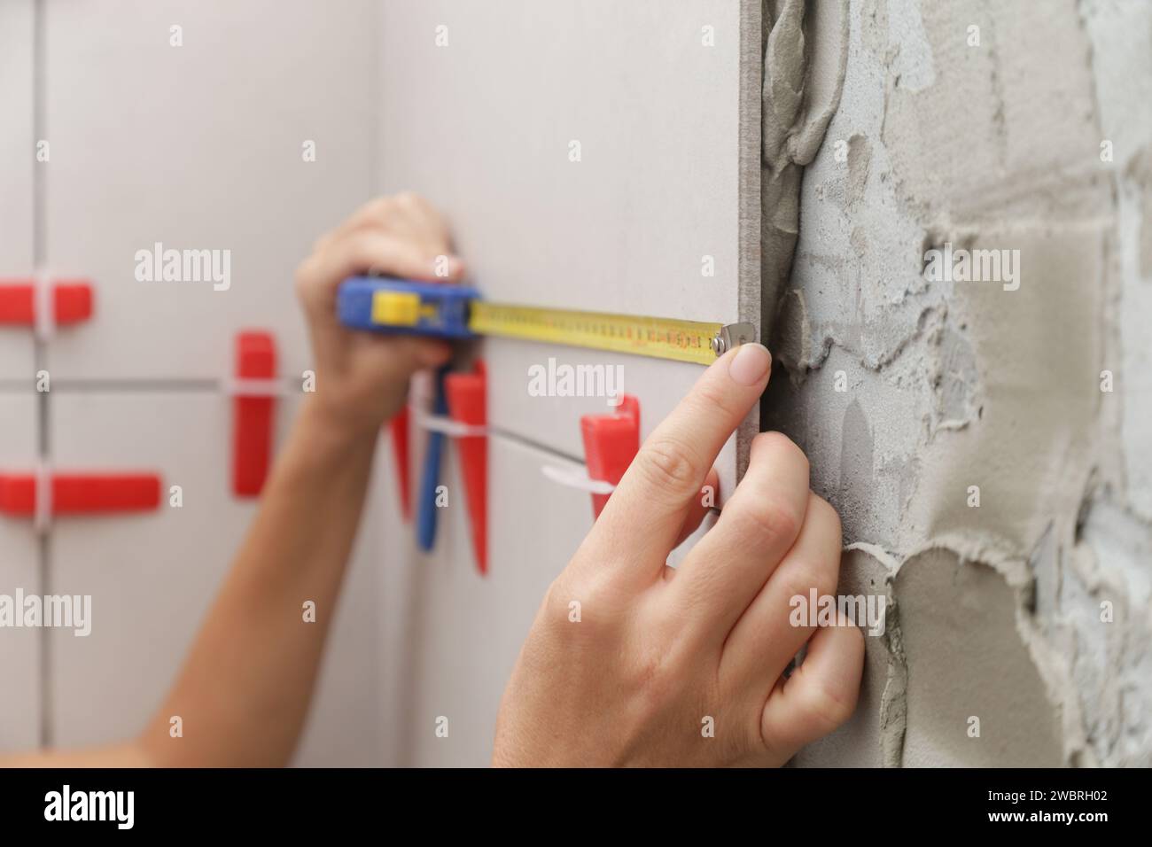 Woman tiling bathroom walls, using tape measure for measuring length. Process of installation of