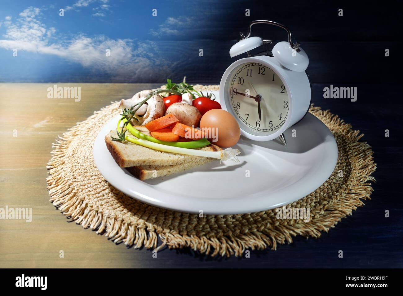 Intermittent fasting, plate with an alarm clock and partly filled with food, diet concept of interval eating in a time slot one third of the day, back Stock Photo