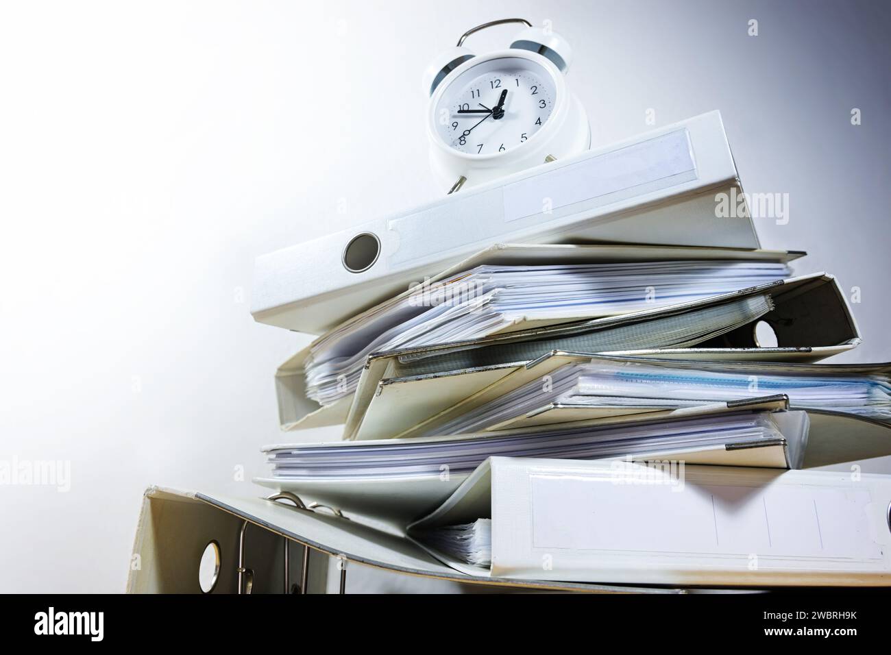Alarm clock on stacked ring binders against a gray background threatened to deadline ultimatum, business concept for time management and work overload Stock Photo