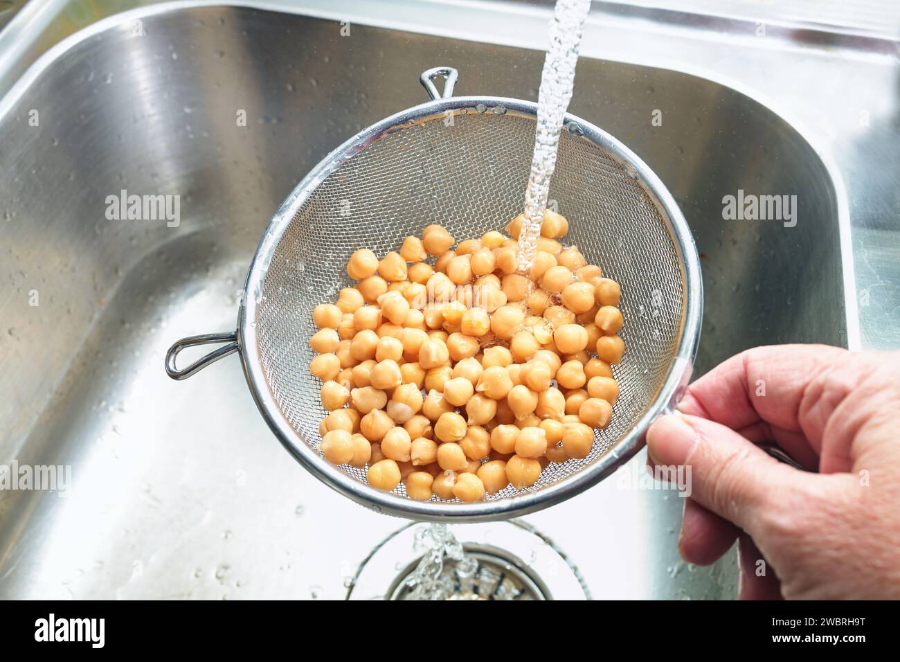 Precooked canned chickpeas are rinsed with water in a sieve over the