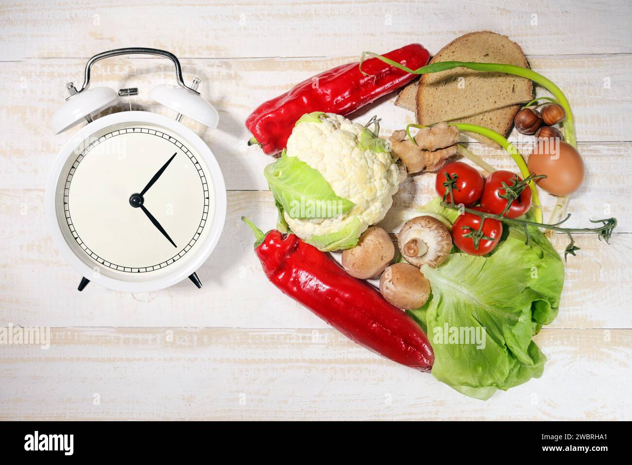 Interval fasting or IF, food products, and an alarm clock indicate the period of time during which it is allowed to eat, diet concept for losing weigh Stock Photo