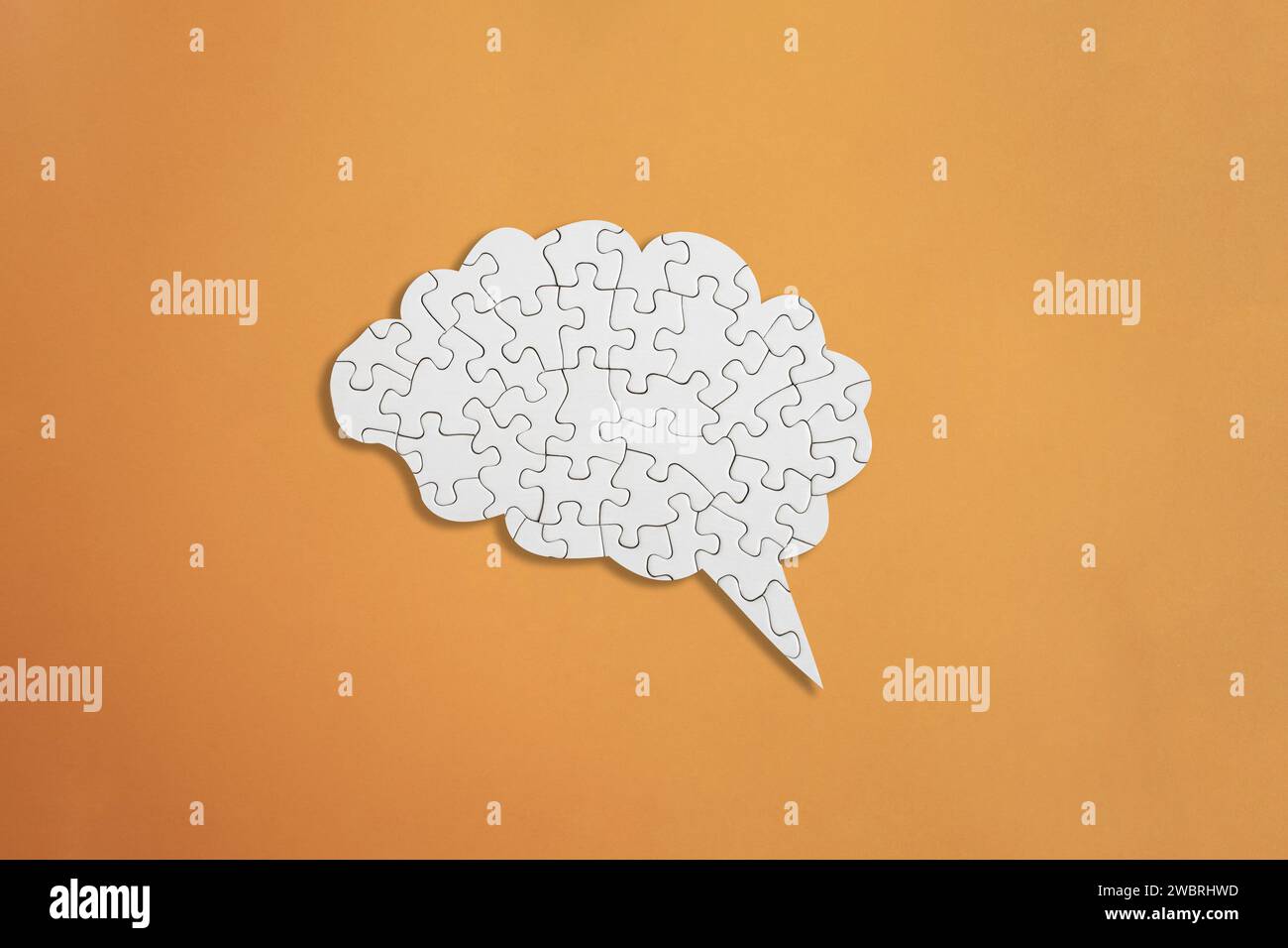 Brain shaped white jigsaw puzzle on orange background, mental health
