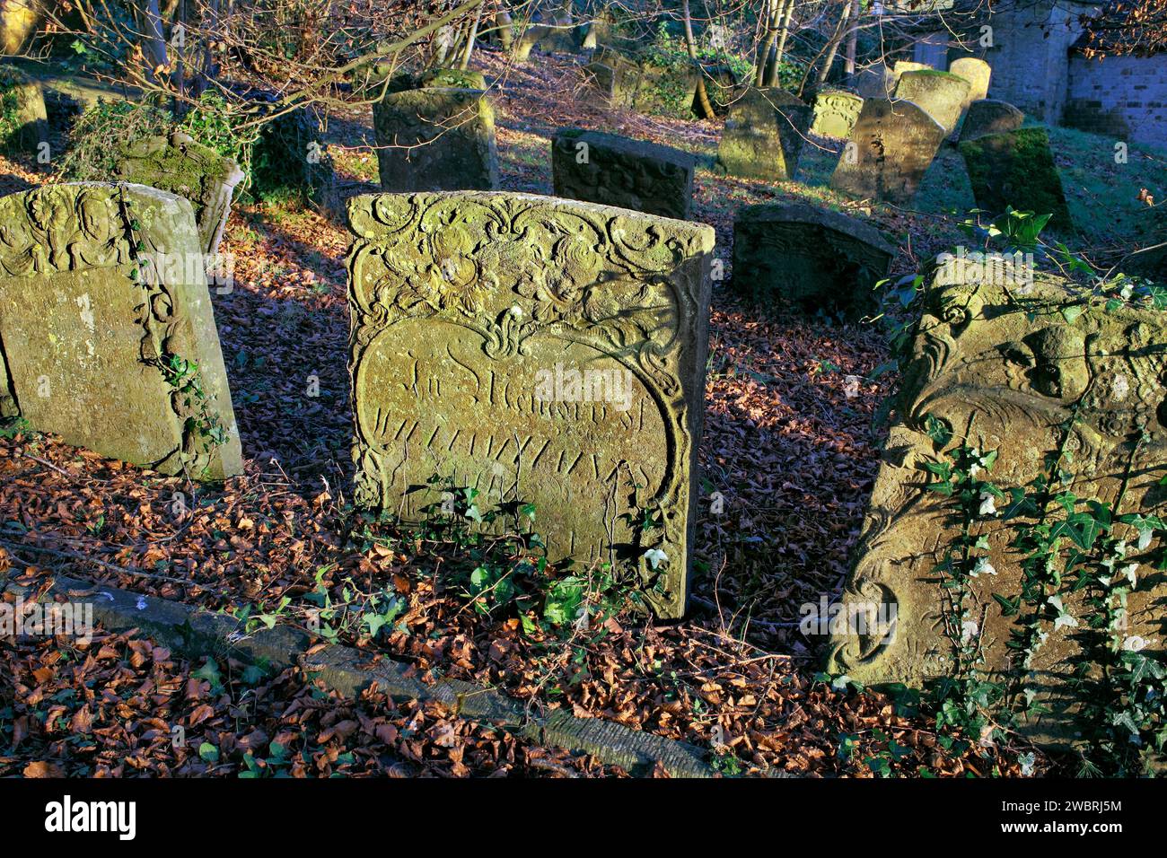 Late afternoon winter sunshine highlights ornate details on old weathered headstones in a church graveyard. Stock Photo