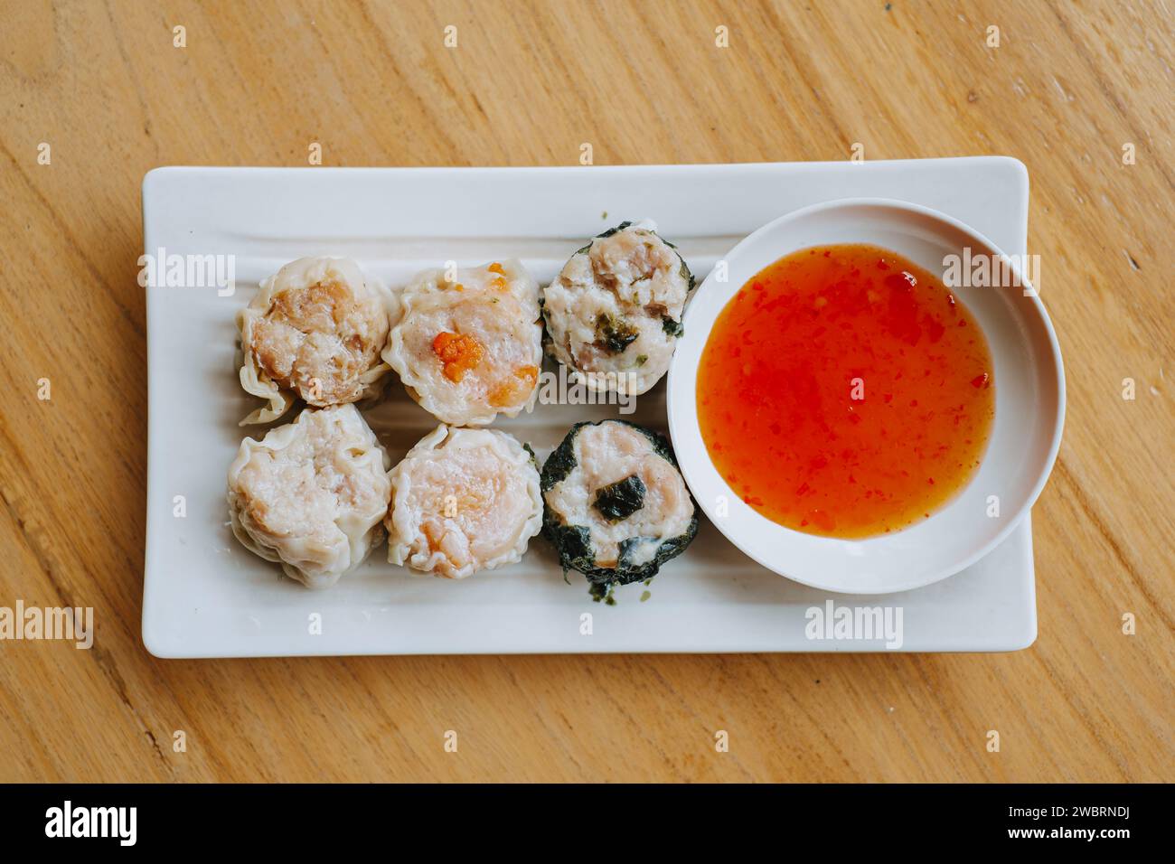 A plate of Dim Sum with chili sauce on wooden table. Flat lay or top