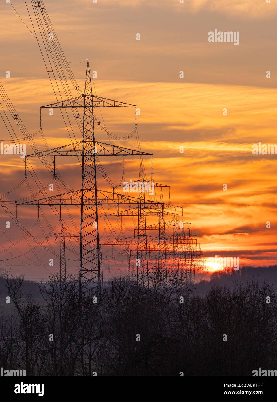 Energy Distribution Network - Electricity Pylons against Orange and Yellow Sunset Stock Photo