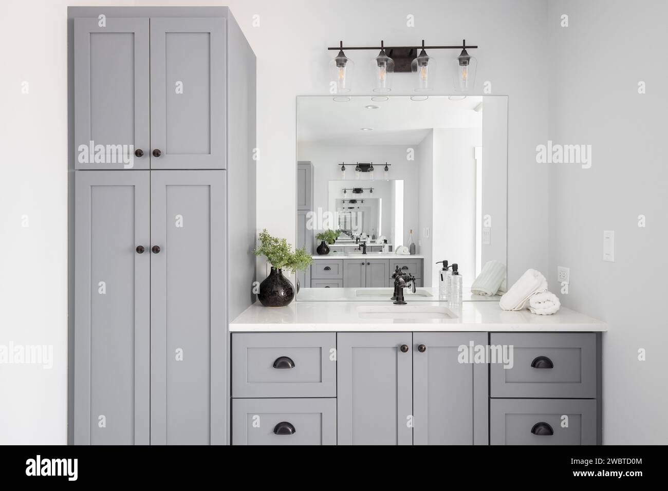 A renovated modern farmhouse bathroom detail with grey cabinets, decorations on a white marble countertop, and rubbed bronze faucet. Stock Photo