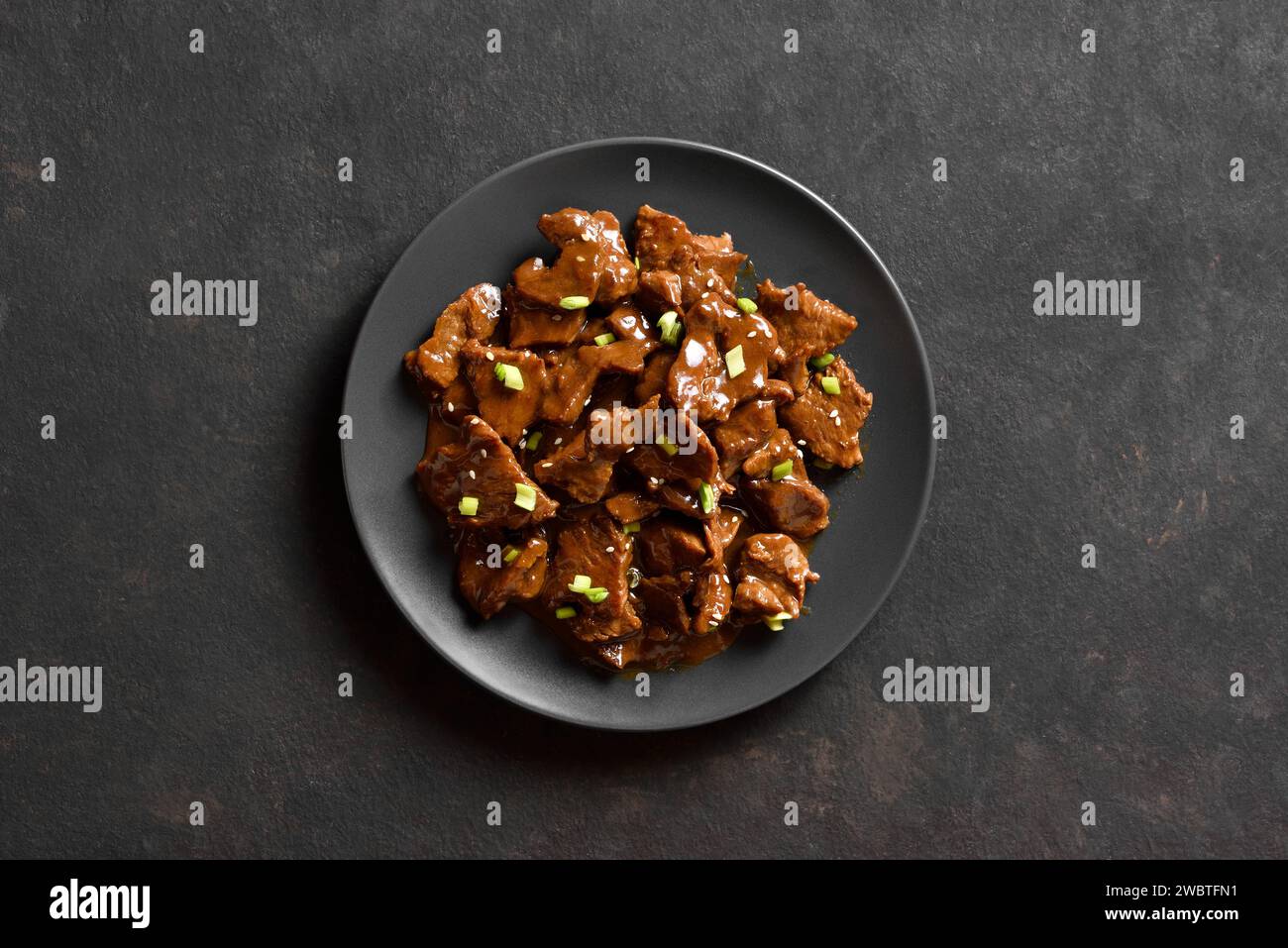 Asian style beef with soy sauce, green onion and sesame seeds on plate over dark stone background. Stir-fried beef dish. Top view, flat lay Stock Photo