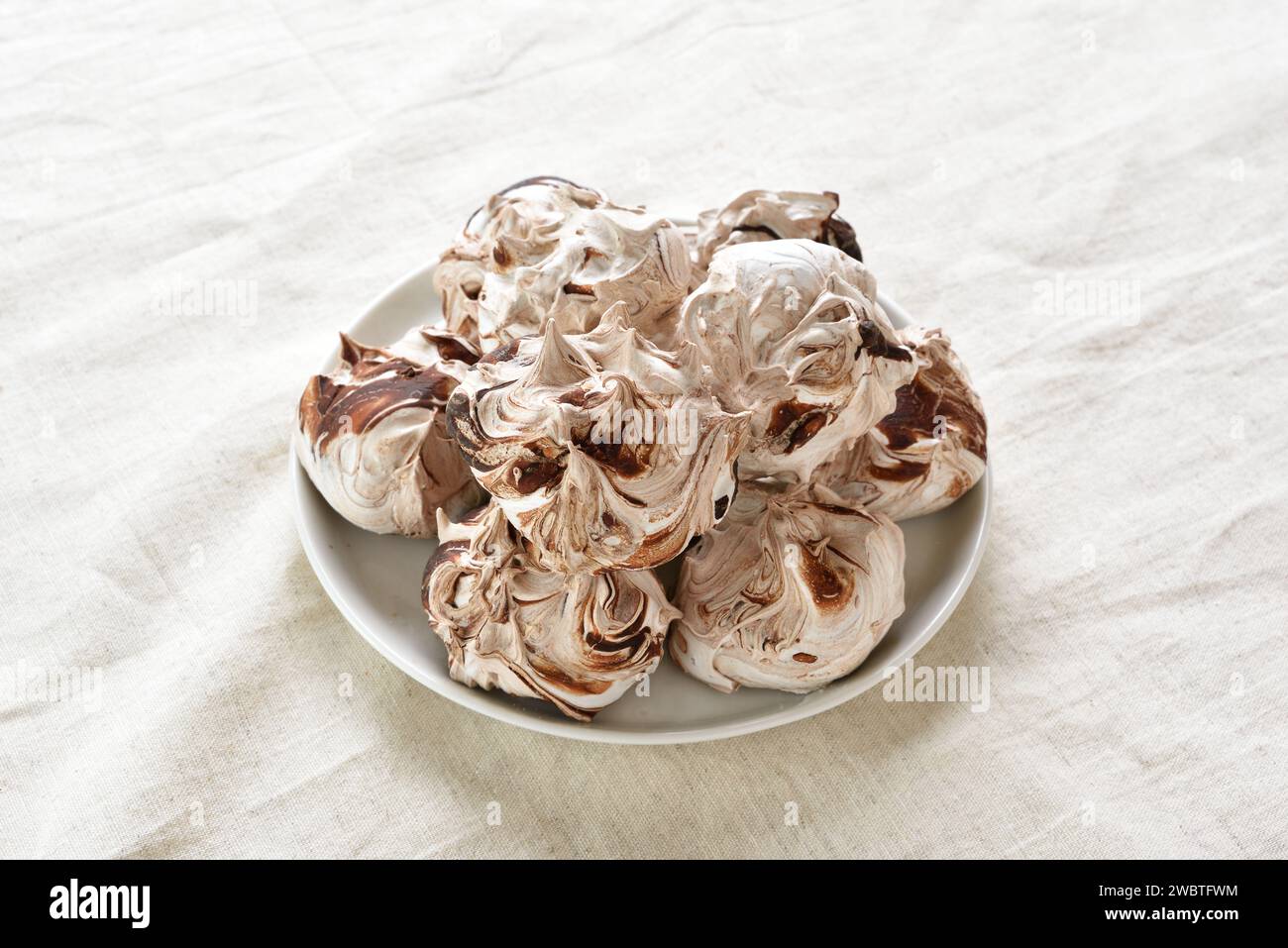 Chocolate meringue cookies on plate over light cloth background. Close up view Stock Photo