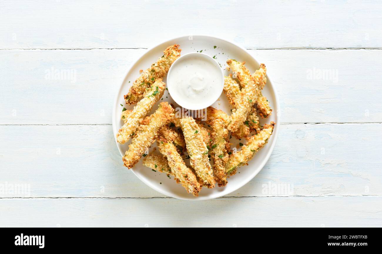 Baked crispy zucchini fries with dipping sauce on plate over light wooden background with free space. Top view, flat lay Stock Photo
