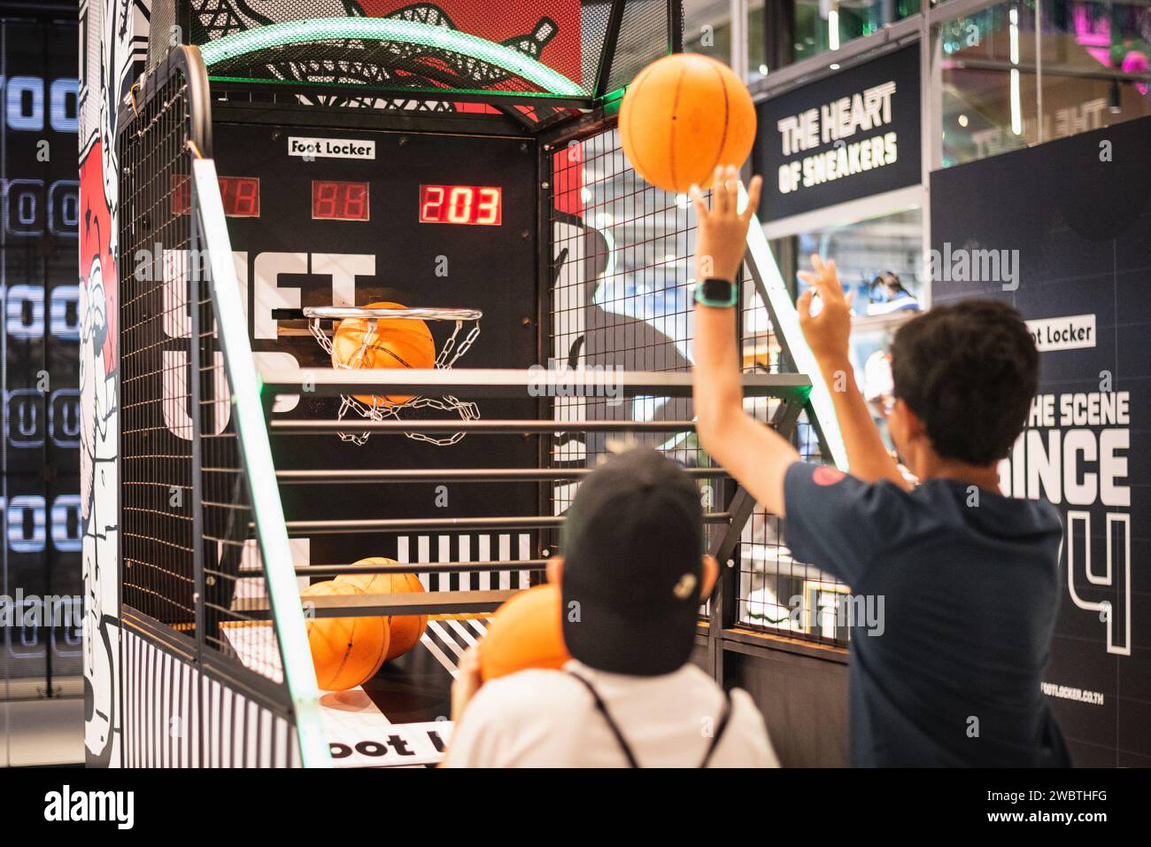 Bangkok, Thailand - December 17, 2023: two boys play basketball arcade game machine at Foot Locker store at EmSphere shopping mall. Stock Photo