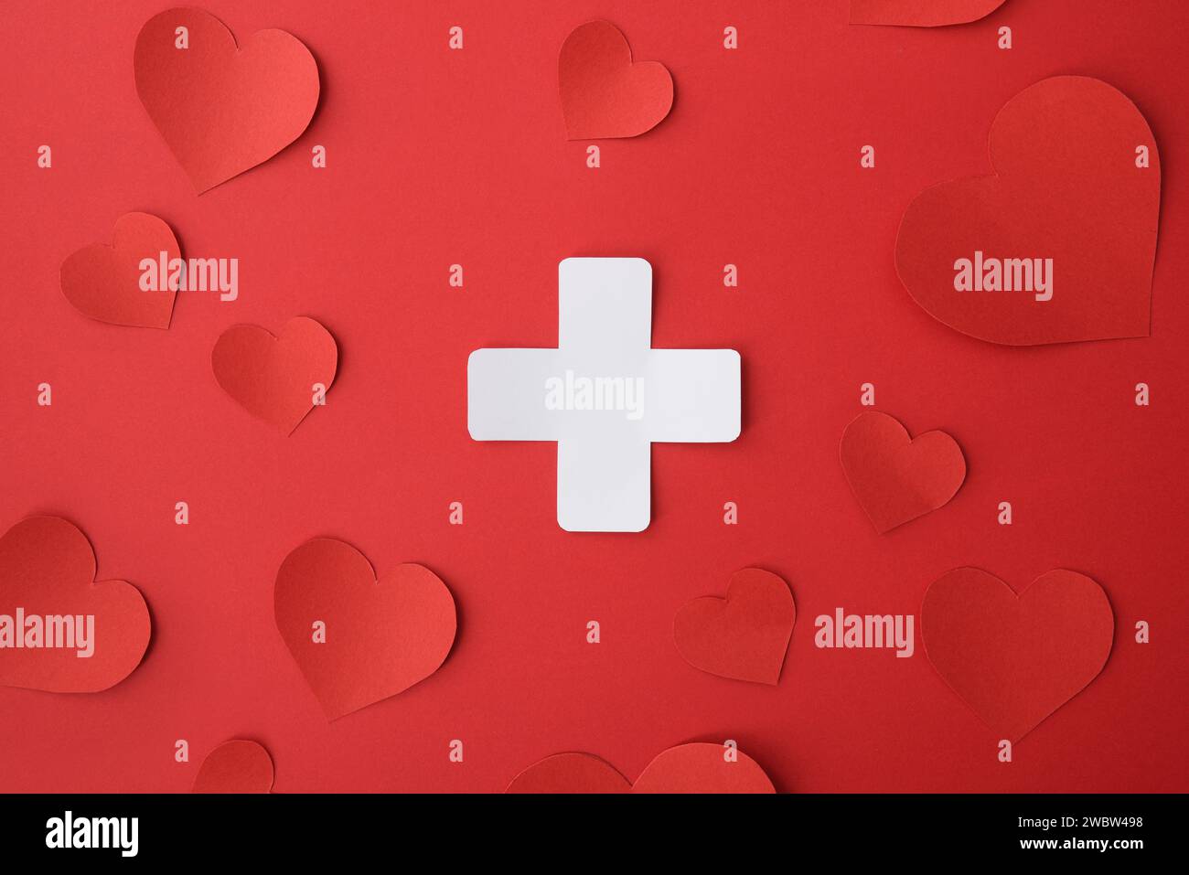 Conceptual medicine symbol with cross shaped paper cutout isolated in the center on red background. Stock Photo