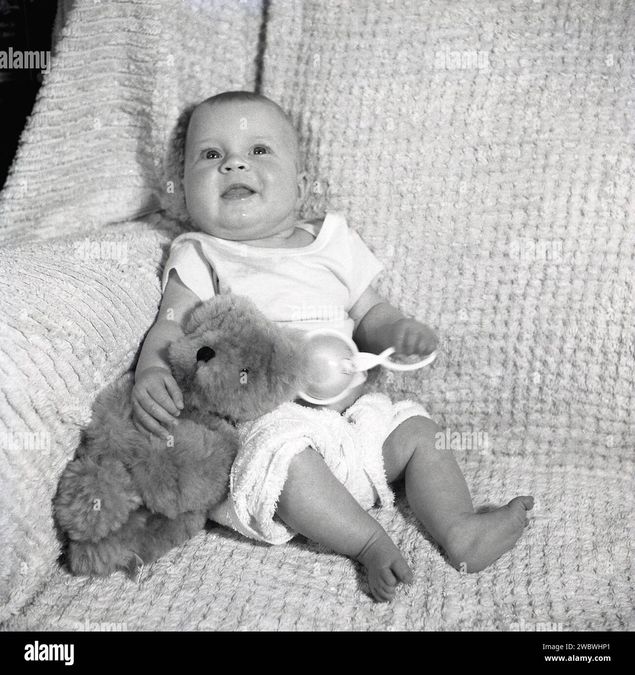 1950s, historical, a chirpy baby sitting on a cotton covered sofa, hand
