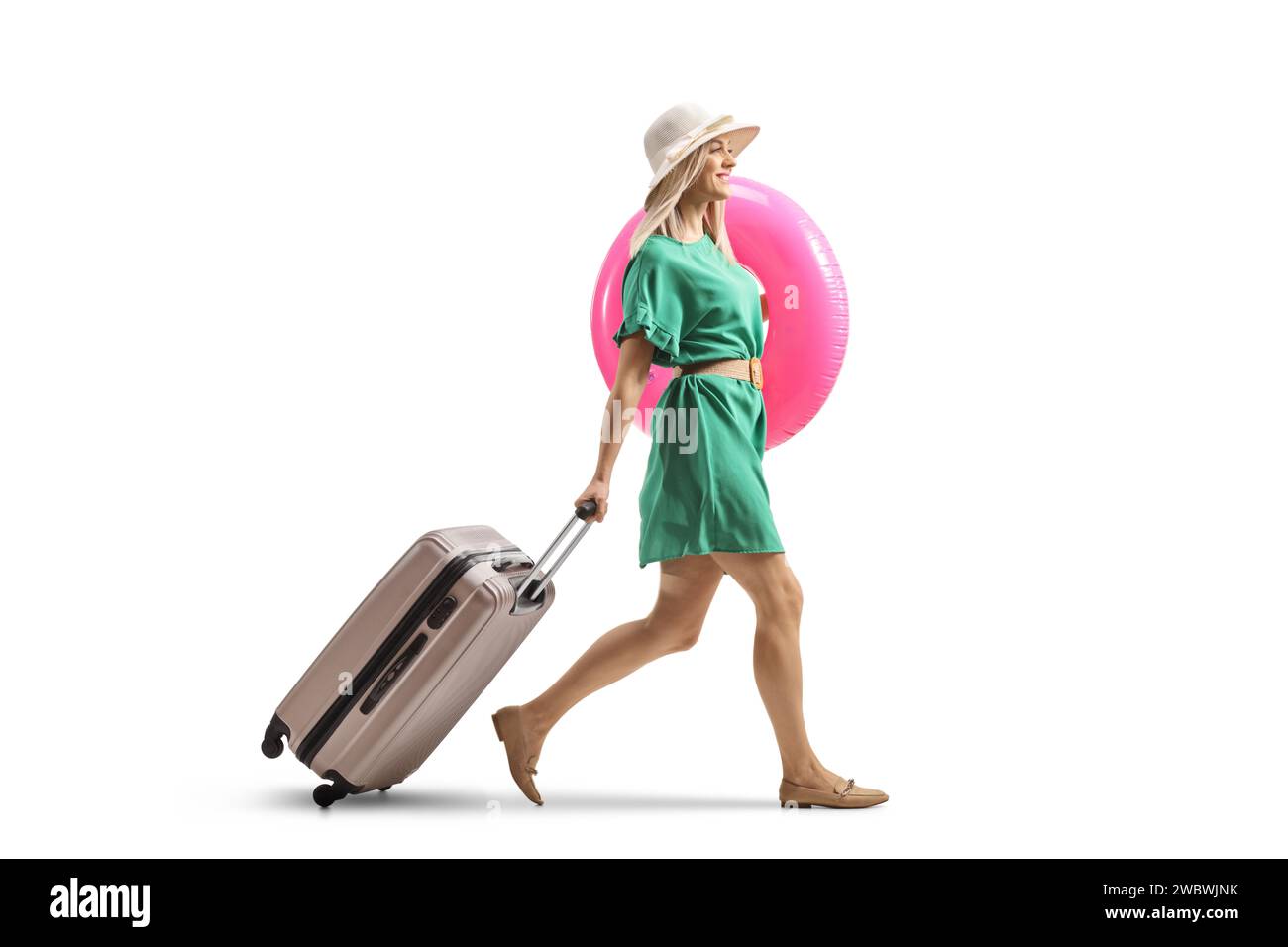 Full length profile shot of a young lady with a suitcase walking and carrying a swimming ring isolated on white background Stock Photo