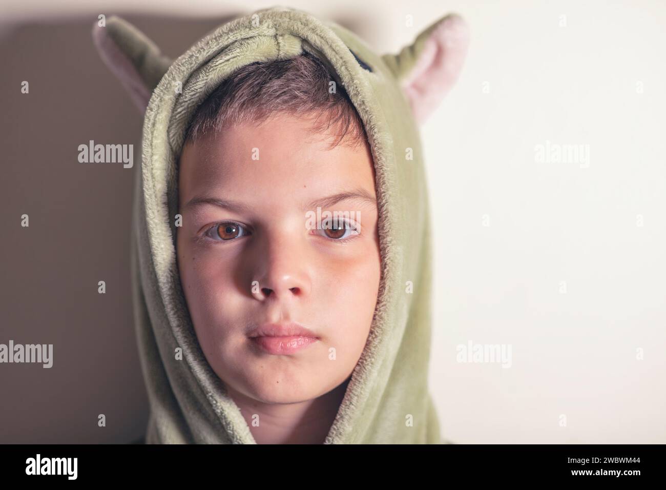 Headshot, portrait of a 9yearold boy in the sleeping gown standing against a wall Stock Photo