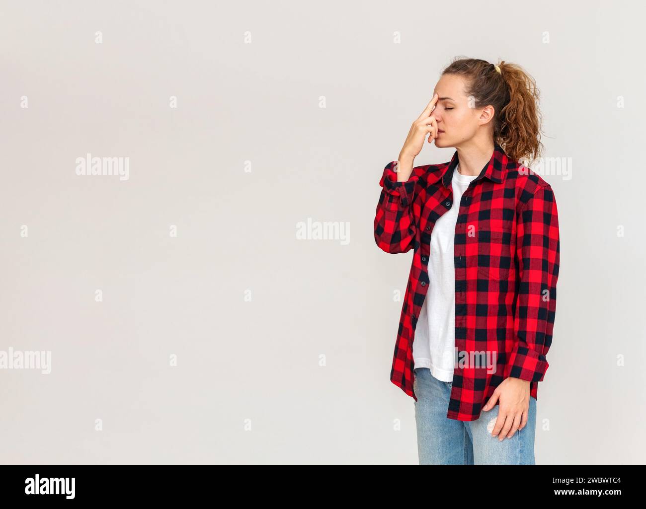Woman in red shirt stands in front of simple background and doing breathing exercise. Touching bridge of the nose with finger. Coping with stress. Str Stock Photo