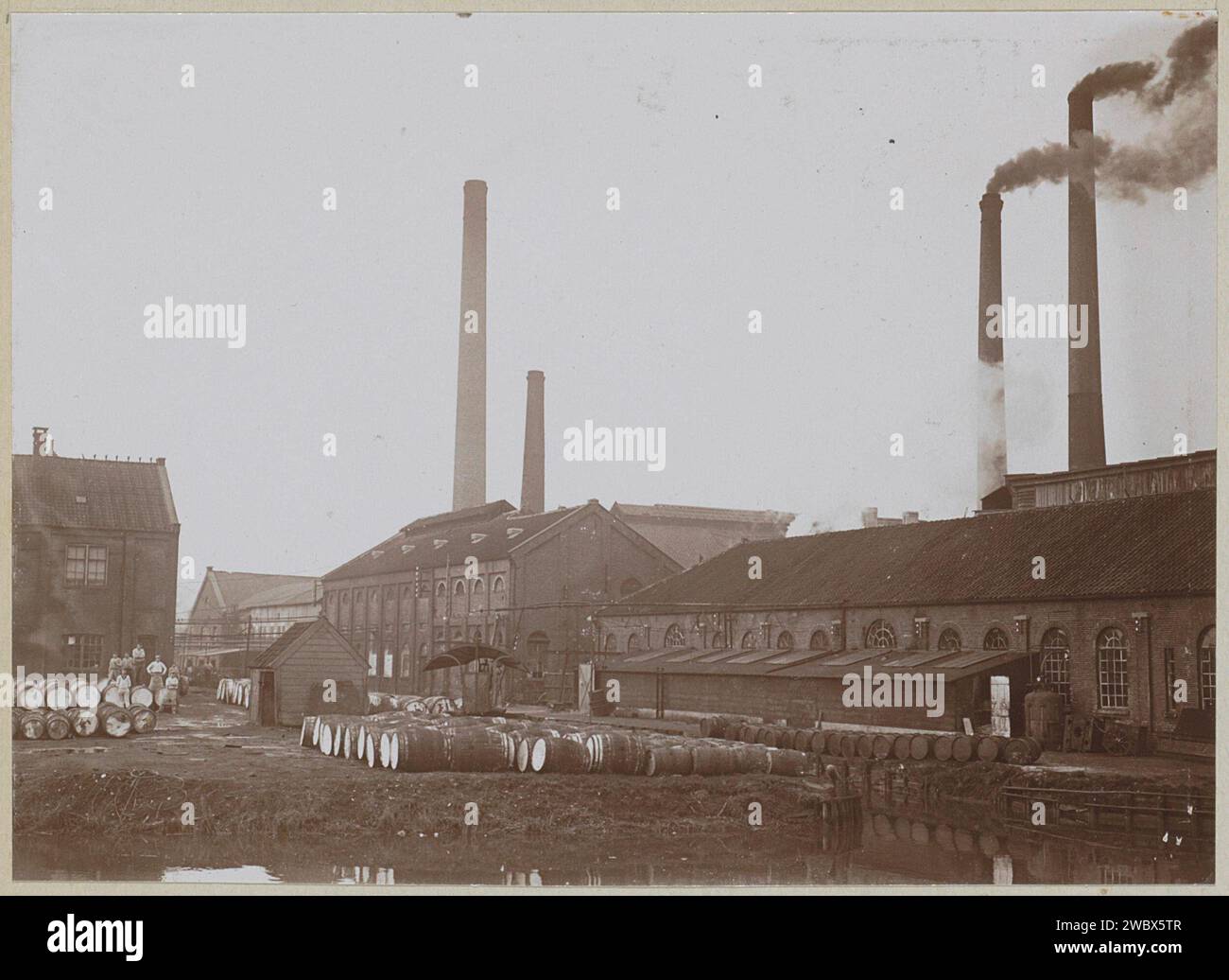 Exterior of factory buildings and smoking chimneys, with wooden barrels in the foreground, anonymous, c. 1900 - c. 1910 photograph Part of Family Album with photos of Wijnhandel Kraaij & Co. Bordeaux-Amsterdam.  photographic support  factory-building. smoke-stack. wooden container: barrel, cask (+ wood and other phytogenic material) Stock Photo