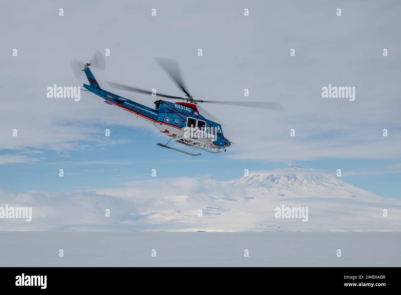 McMurdo Station, Antarctica. 28 December, 2023. A National Science Foundation helicopter flies past Mt. Erebus near the U.S. Antarctic research station, December 28, 2023 in McMurdo Sound, Antarctica.  Credit: PO3 Ryan Graves/U.S. Coast Guard/Alamy Live News Stock Photo