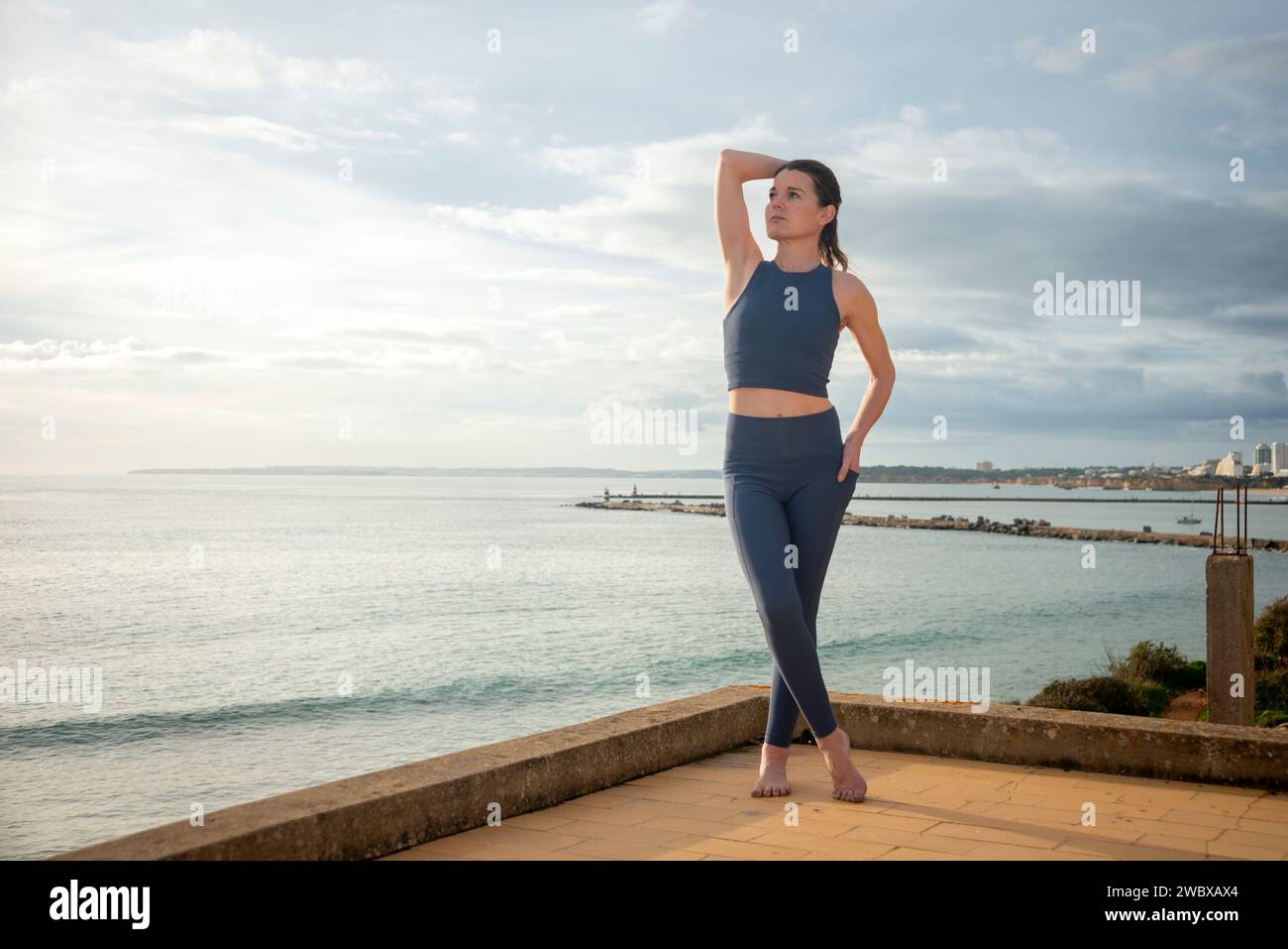 Sporty woman standing by the ocean, relaxing after workout, hand on head Stock Photo