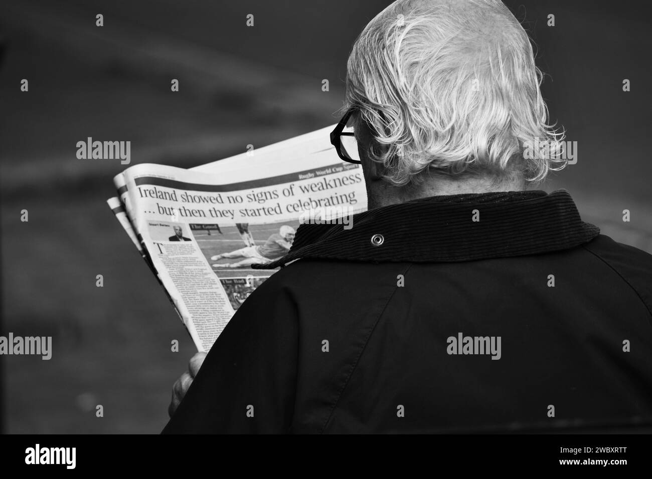 Ross On Wye, Herefordshire, England Sept 24 2023: Man with grey hair and glasses sat down reading a newspaper on a public bench. Black and white photo Stock Photo