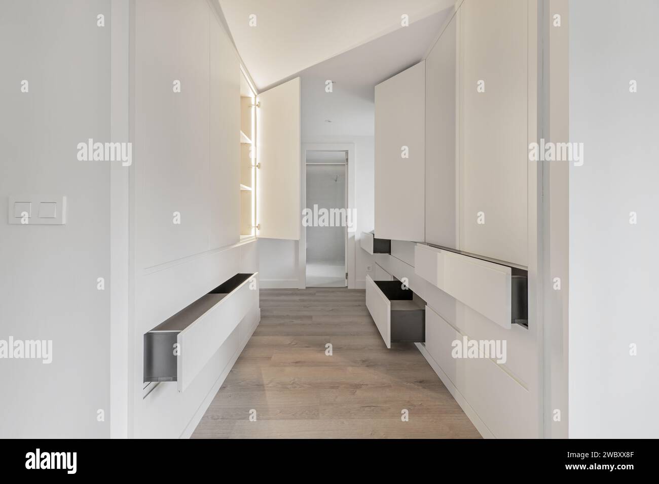 A dressing hallway that leads to an en-suite bathroom with open drawers and doors in the closets and LED lights inside Stock Photo