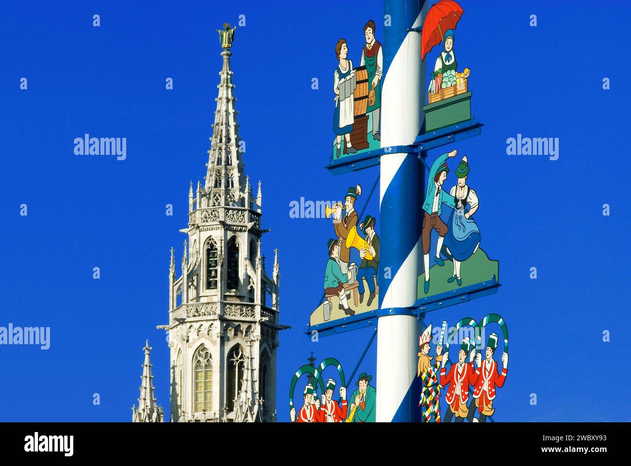 Maypole on Viktualienmarkt with musicians, dancing couple, market woman, waitress of Oktoberfest, tower of new town hall in background, Munich, Bavari Stock Photo