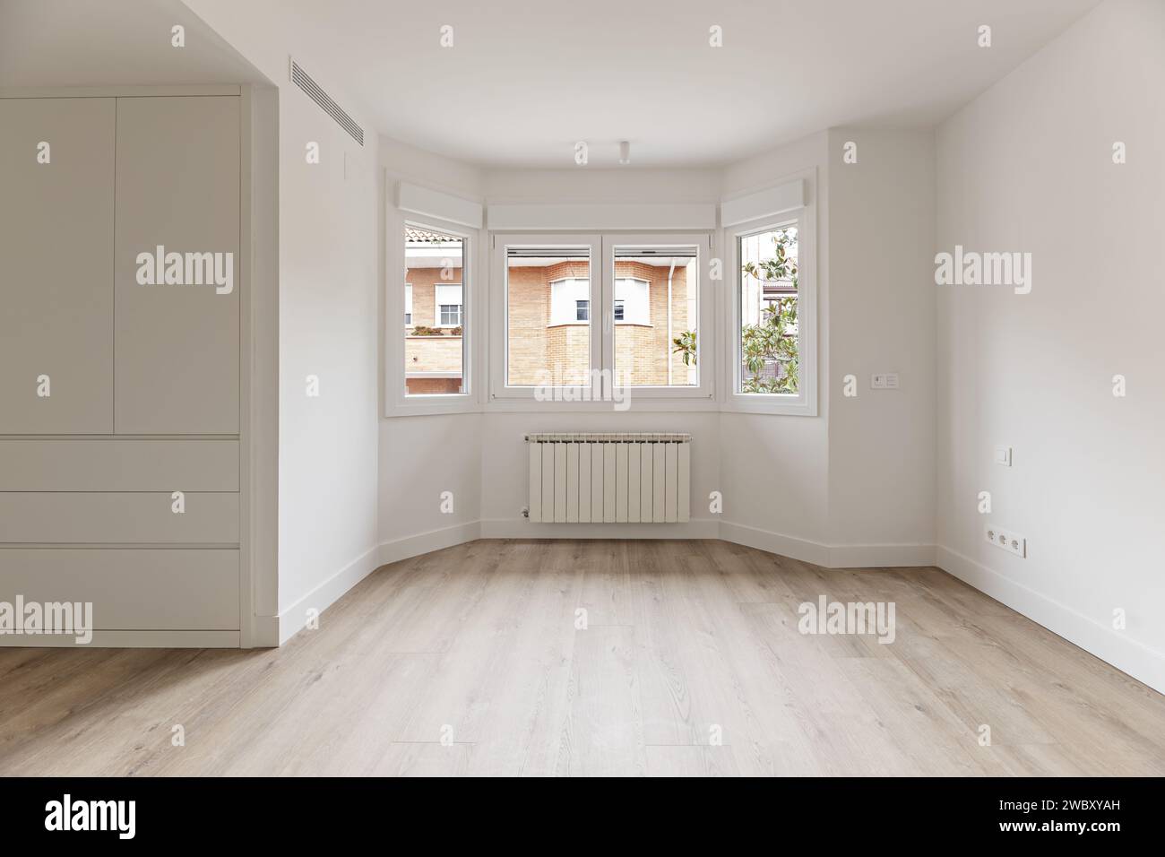 A newly renovated room with white wooden cabinets, a large gallery with white aluminum windows, radiators underneath and light wooden flooring Stock Photo