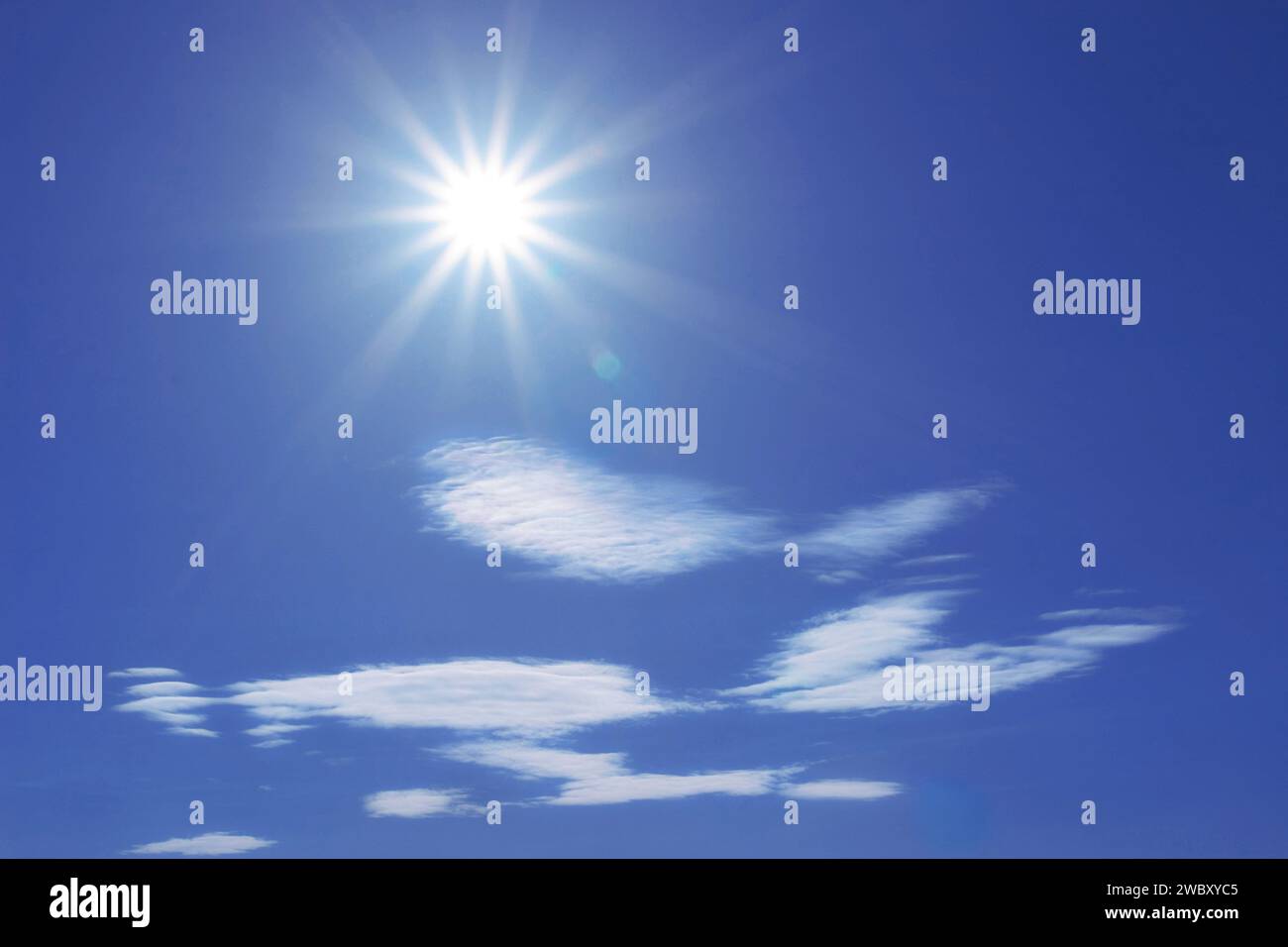 sun in blue sky with some white lenticular clouds Stock Photo