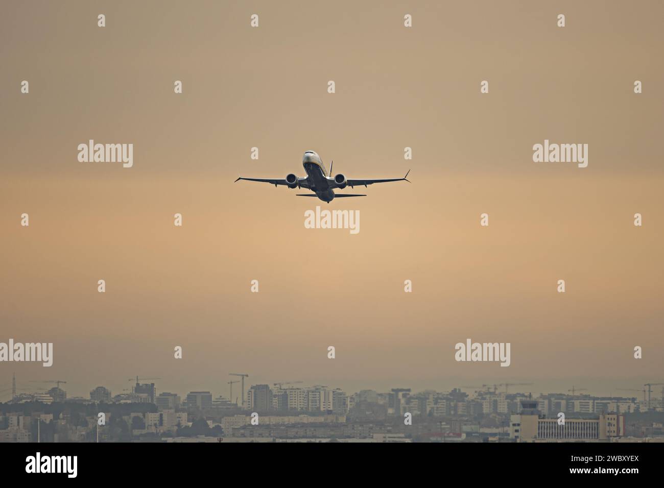 Flight of a commercial airplane over a city on a warm-colored afternoon Stock Photo