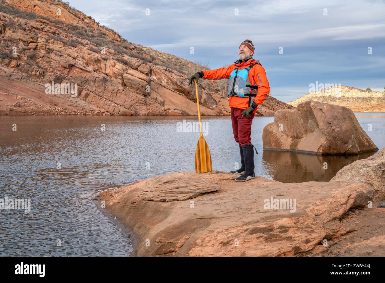 senior male paddler with a wooden canoe paddle on a rock shore of a mountain lake - Horsetooth Reservoir in fall or winter scenery Stock Photo