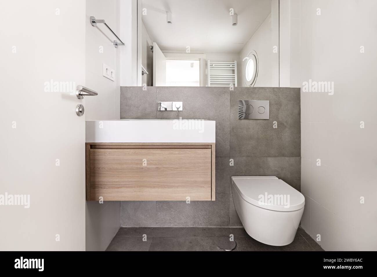 Front image of a small bathroom with marble effect tiled walls, integrated wall mirror, and towel rack on the wall Stock Photo