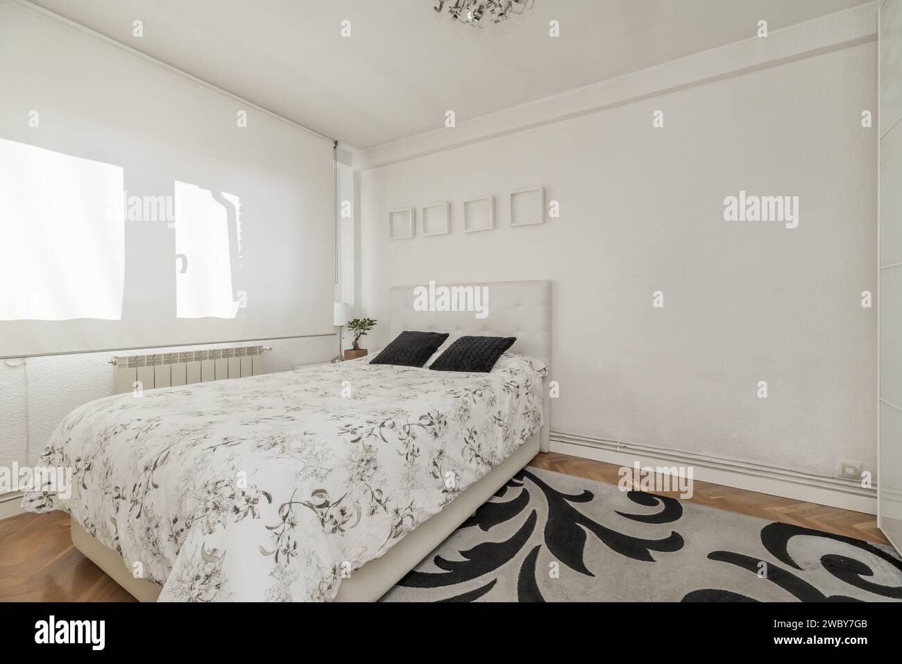 A bedroom with a double bed and a large white fabric blind covering the windows Stock Photo
